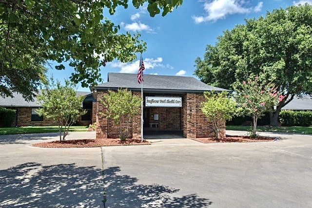 A small brick post office with an American flag, surrounded by trees under a blue sky.