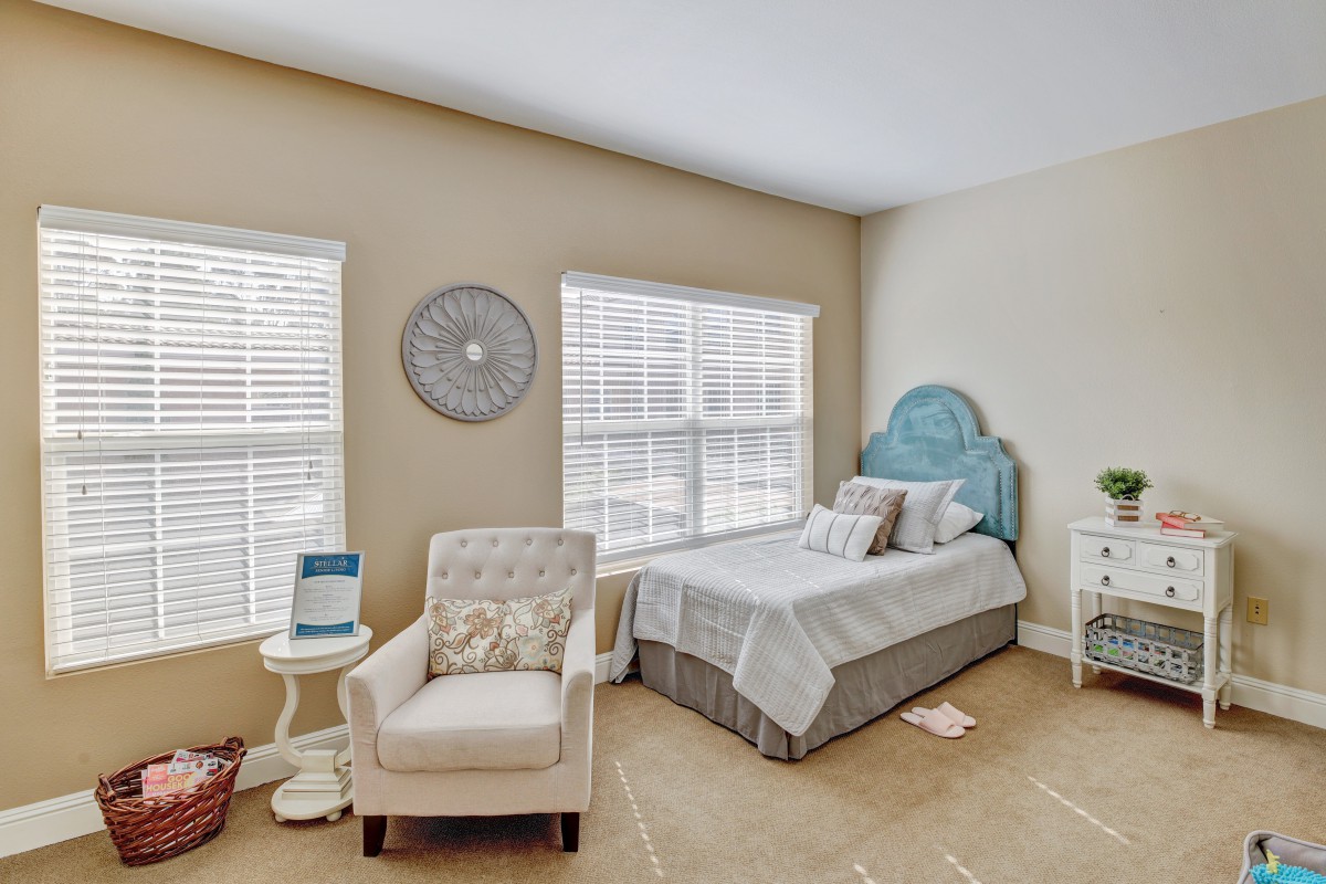 A cozy bedroom with a single bed, armchair, and two large windows letting in natural light.