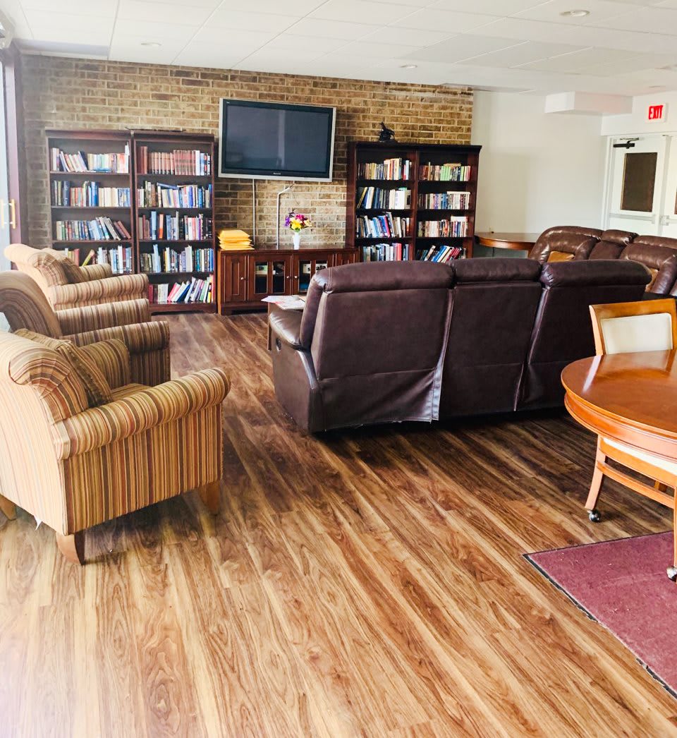 A cozy library seating area with leather sofas and armchairs, surrounded by bookshelves and a TV.