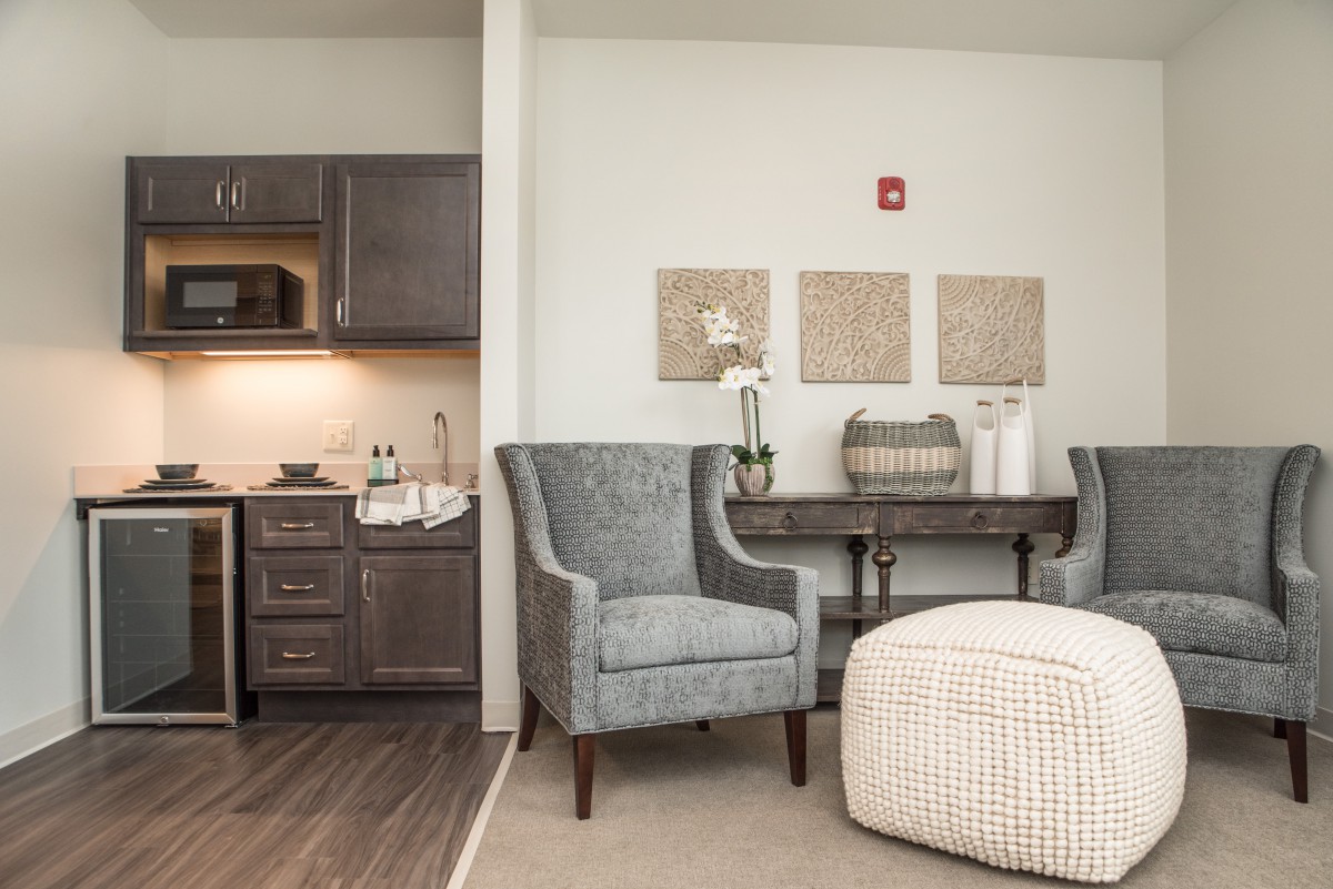 A cozy living space with modern decor, featuring a kitchenette, armchairs, and a small dining table.