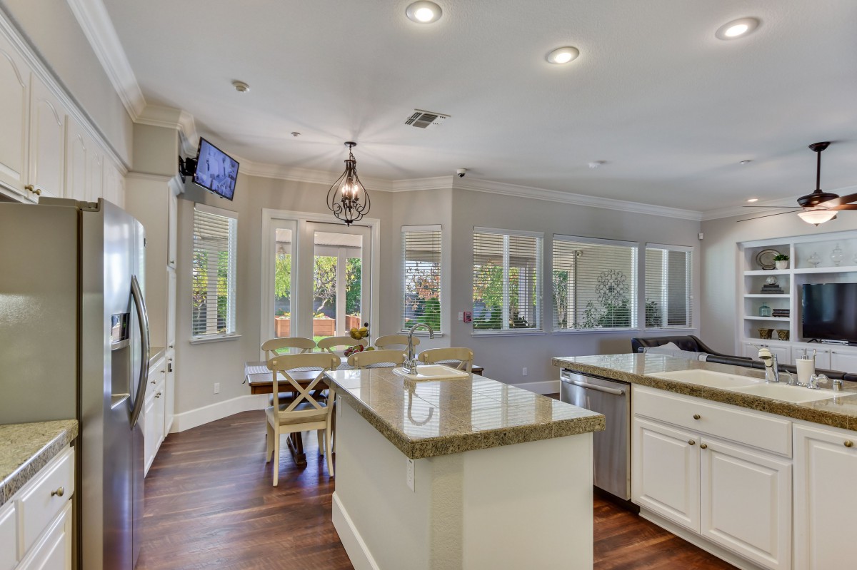 A spacious modern kitchen with an island and dining area, featuring large windows and wooden floors.