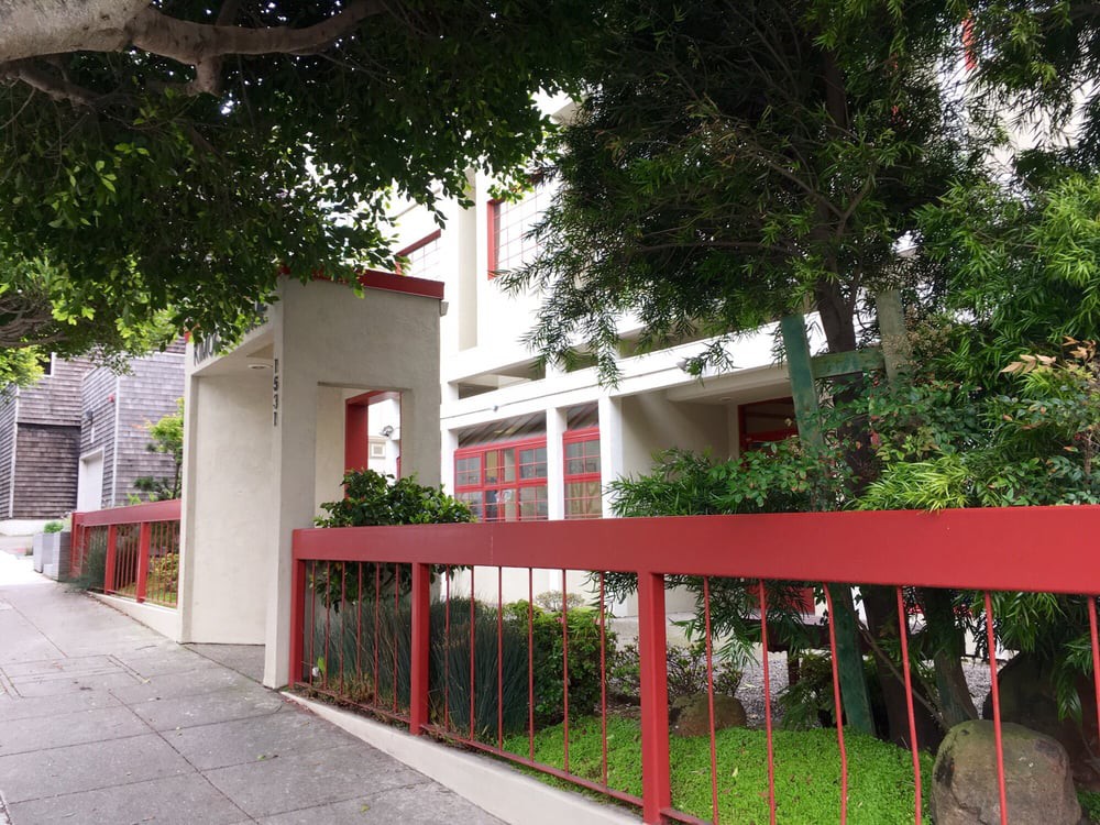 A modern house with a red fence and lush greenery.