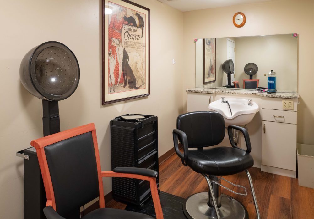 A cozy hair salon interior featuring chairs, a sink, a mirror, and a vintage poster on the wall.