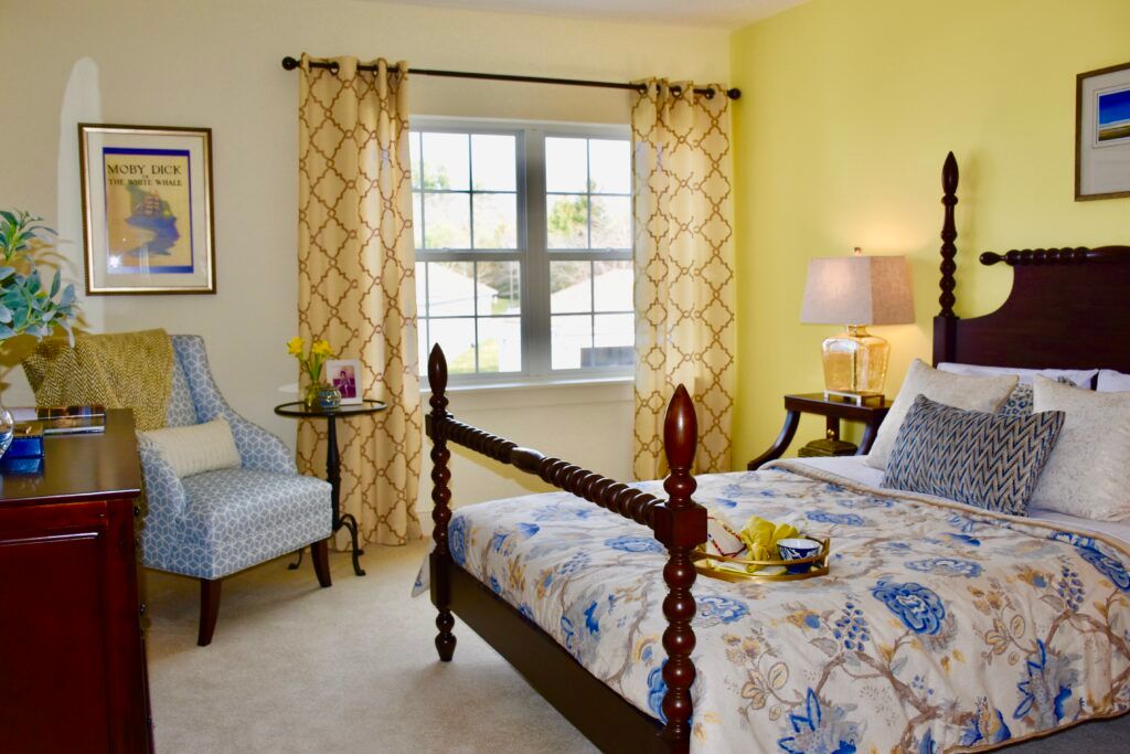 A cozy bedroom with a classic wooden bed, patterned bedding, and bright yellow walls.