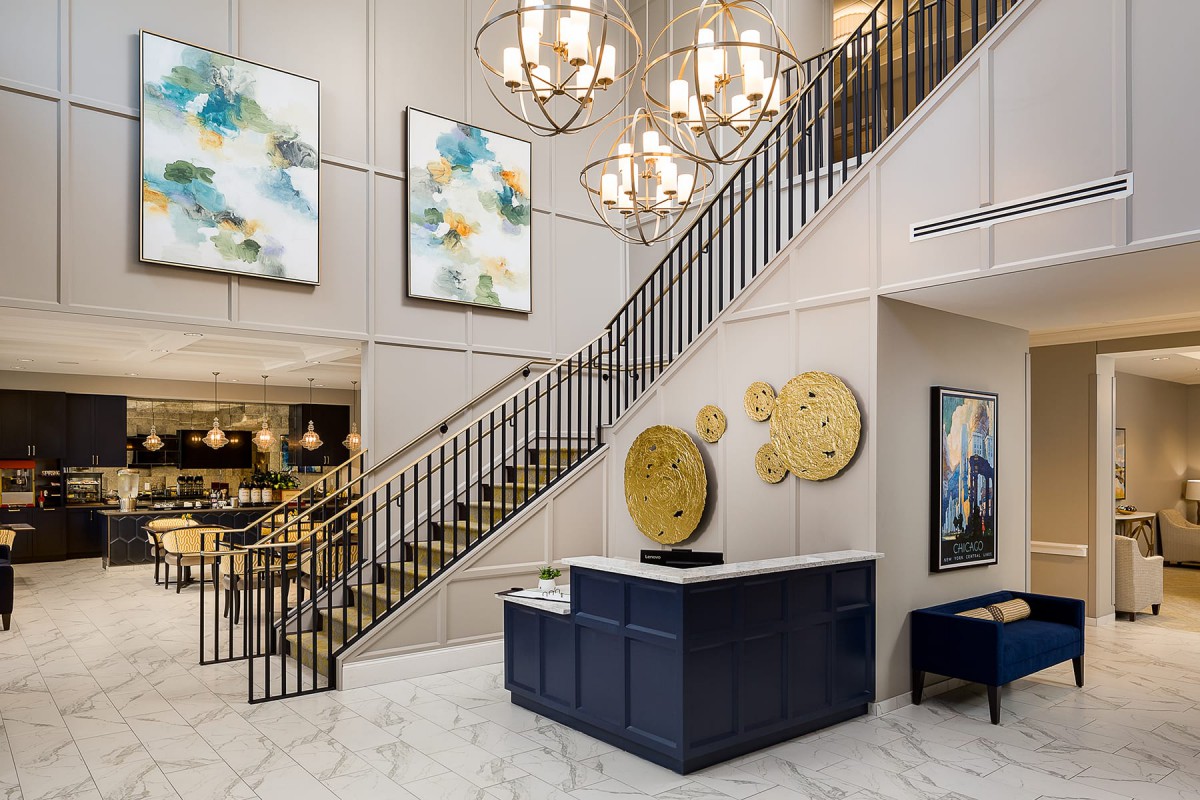 A stylish lobby featuring a grand staircase, elegant chandeliers, and modern artwork.