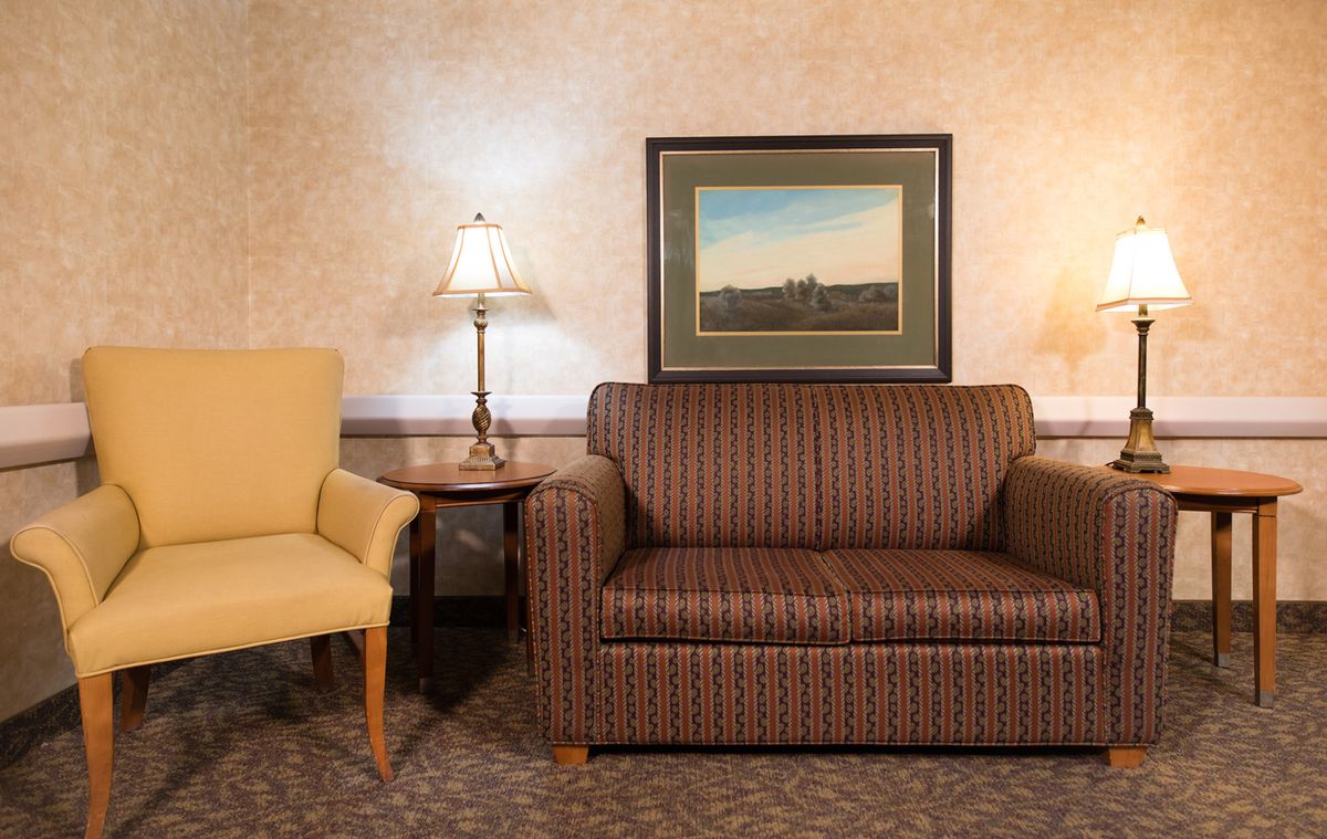 A cozy living room setup featuring a brown striped sofa, a yellow armchair, two table lamps, and framed artwork on the wall.