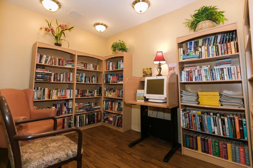 A cozy library corner with bookshelves, a computer, and decorative plants.