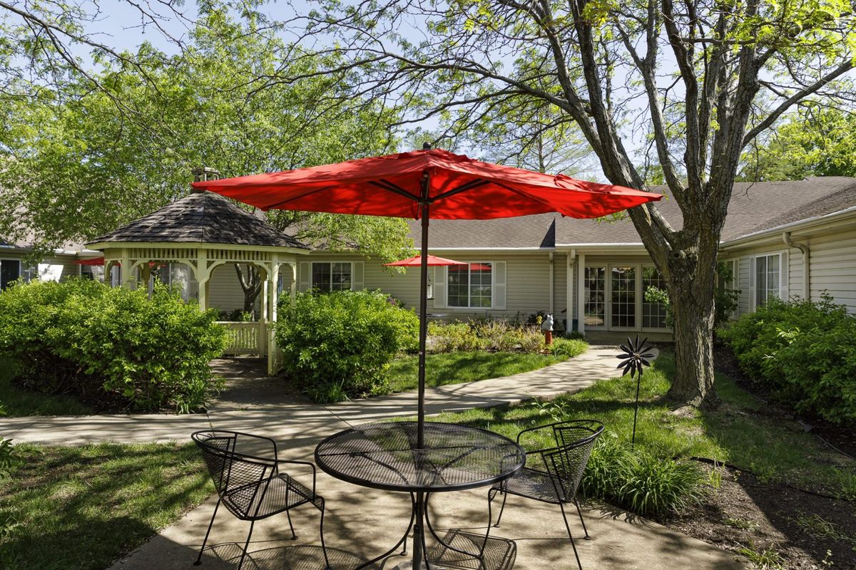 A peaceful garden patio with a red umbrella and metal furniture on a sunny day.