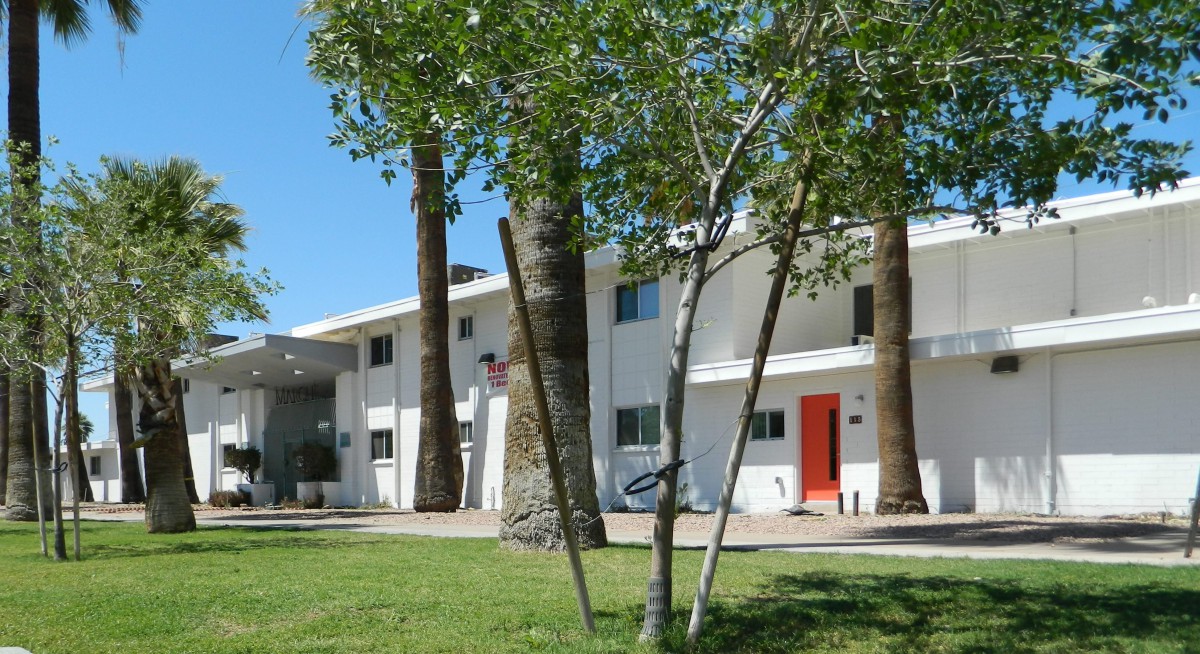 A modern residential building with white walls, red doors, and surrounded by trees on a sunny day.