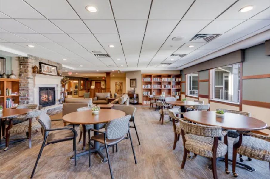 A cozy lounge area with round tables, comfortable seating, a fireplace, and bookshelves.