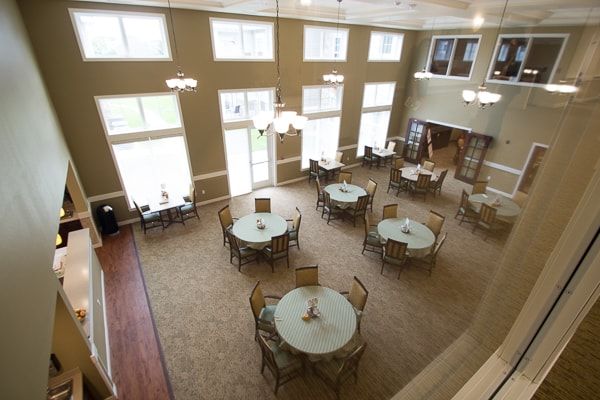 An aerial view of a dining room with round tables and chairs, large windows, and ample lighting.