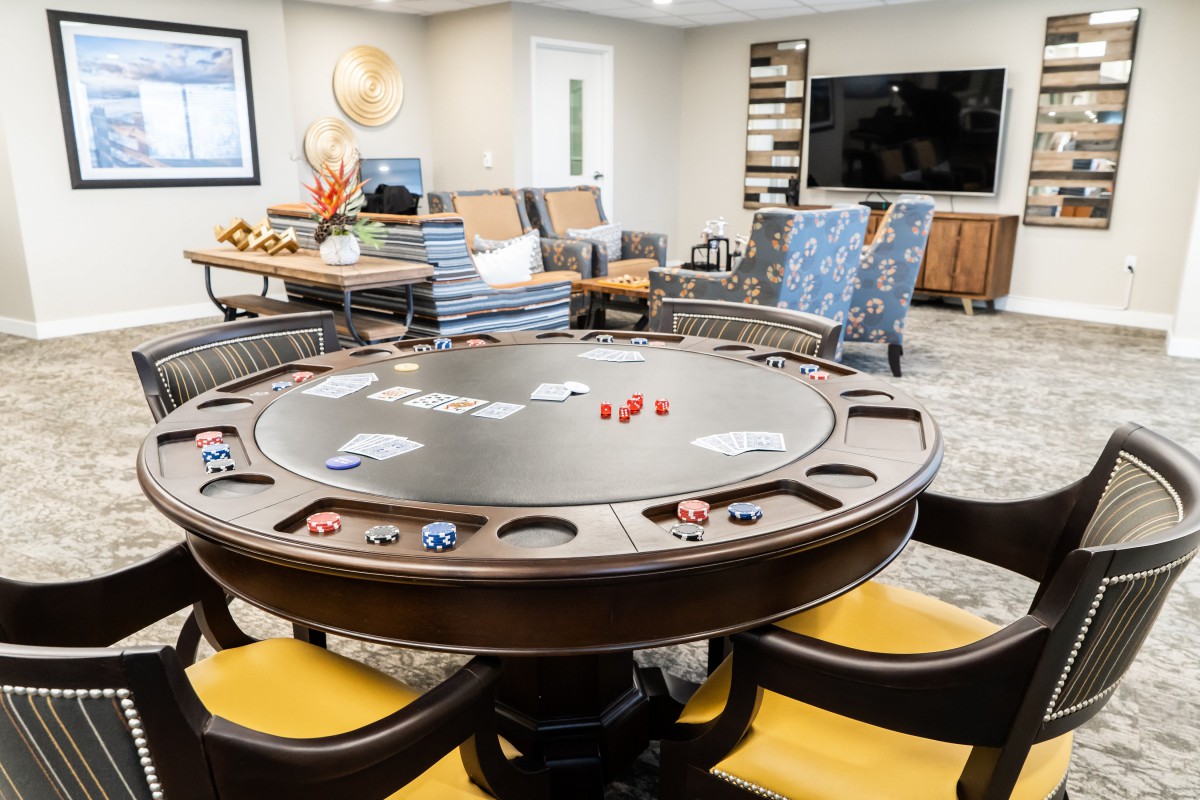 A modern game room featuring a poker table with cards and chips, surrounded by comfortable seating and a large television.