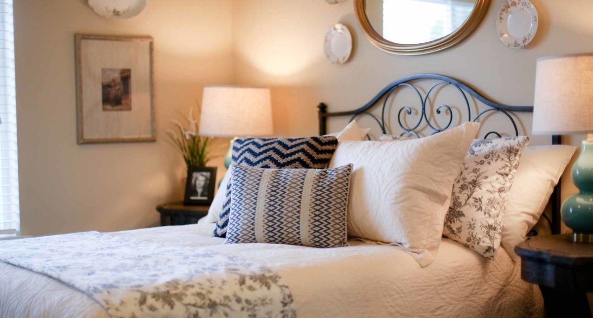 A cozy bedroom interior with decorative pillows and a lamp beside a bed.