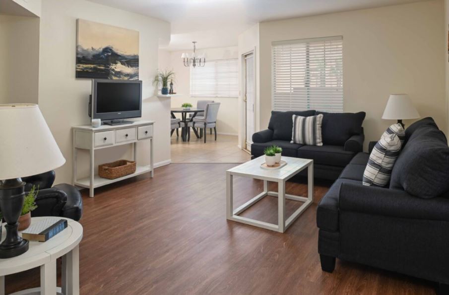 A cozy living room with dark sofas, a white coffee table, and a television on a stand.