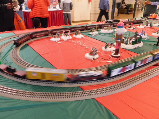 A festive model train set in motion, surrounded by holiday decorations.