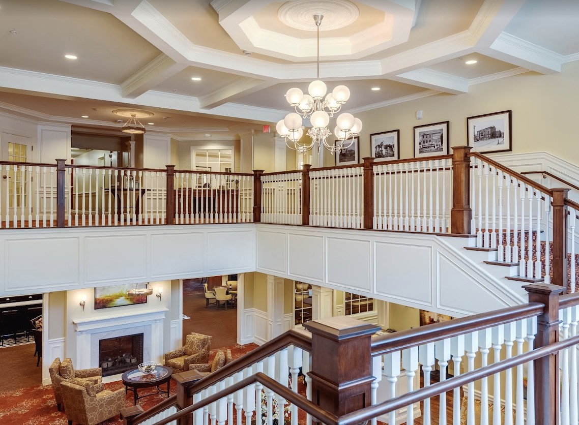 A spacious interior featuring a grand staircase with elegant railing, a chandelier, and comfortable living areas.