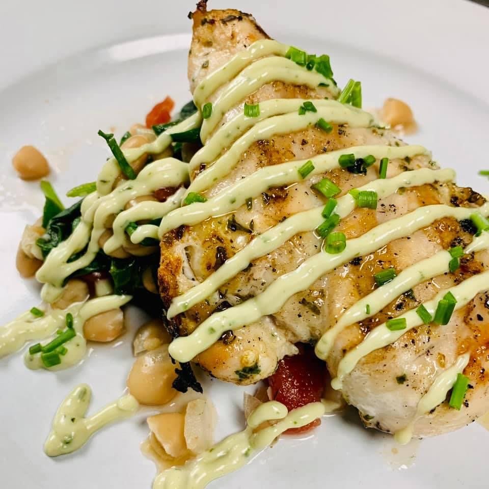 A beautifully plated dish featuring grilled chicken drizzled with a creamy sauce, accompanied by chickpeas and vegetables.