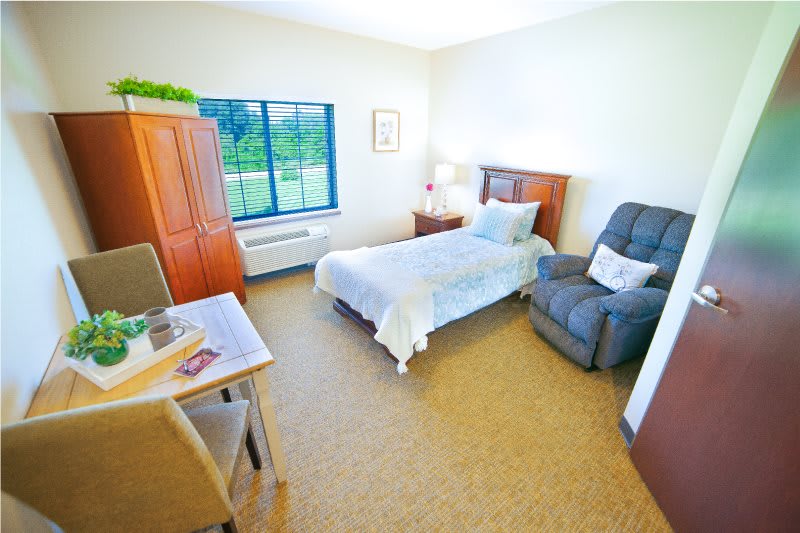 A cozy and well-lit bedroom with a single bed, chair, and window view.