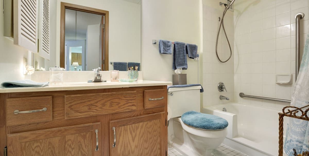 A clean and organized bathroom with wooden cabinets, blue decorative towels, and a shower area.