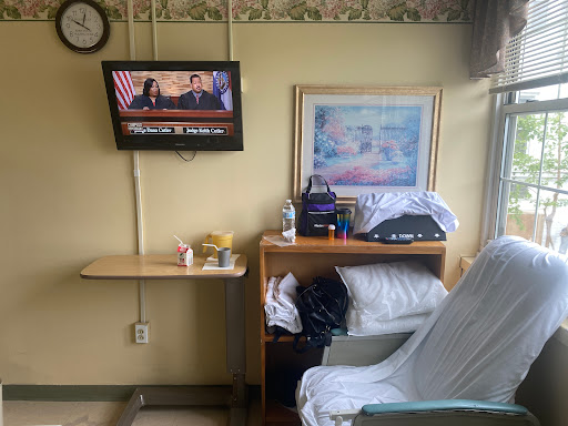 A view of a hospital patient room featuring a television, a bed, and some personal items.