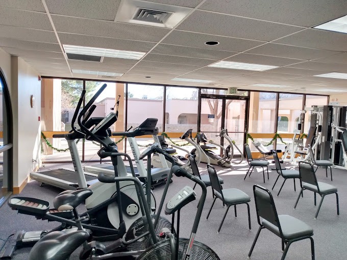 A spacious gym area with various exercise equipment including treadmills and stationary bikes, accompanied by several chairs near large windows.