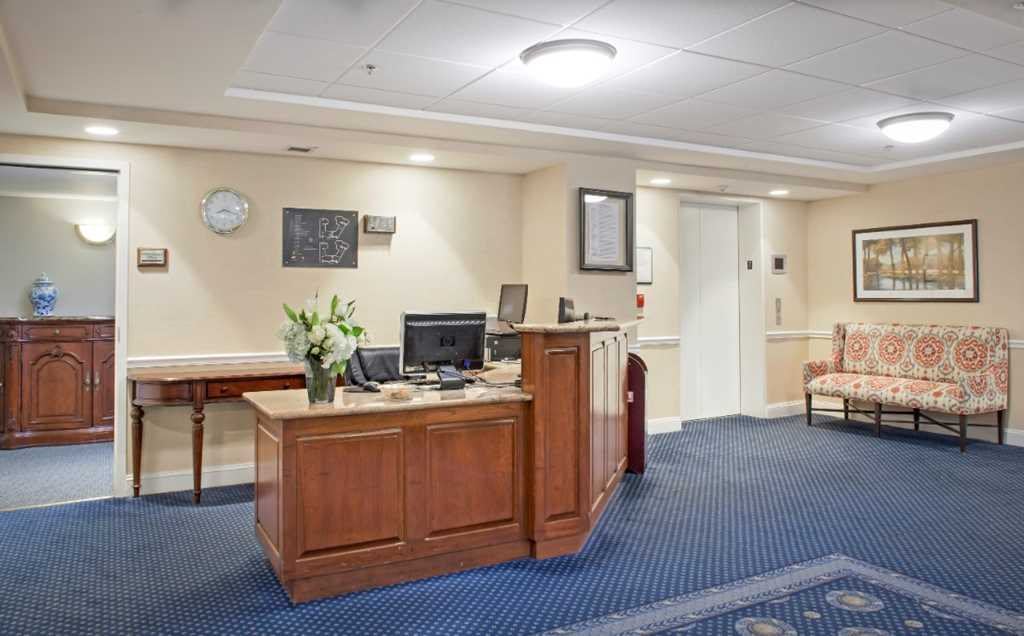 A clean and tidy reception area with a wooden desk, computer, and floral arrangement.