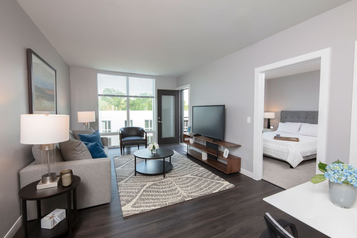 A modern living room with a view into the adjacent bedroom, featuring stylish furniture and decor.
