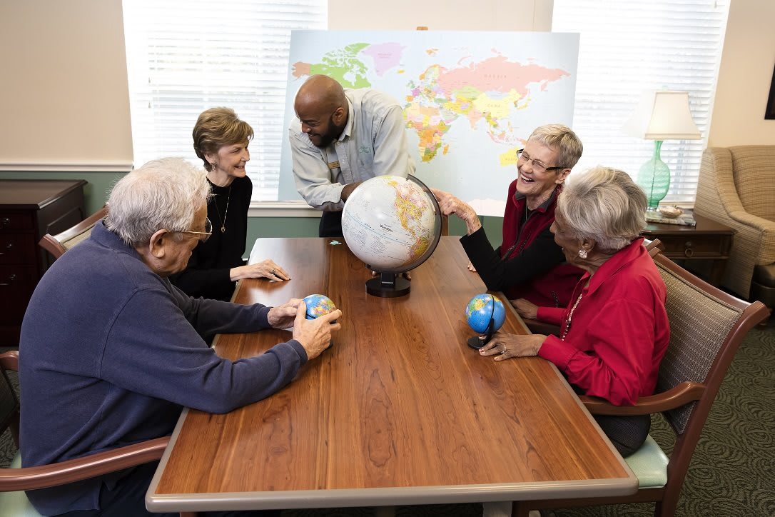 A group of seniors engaging in a geography discussion using globes and a world map.