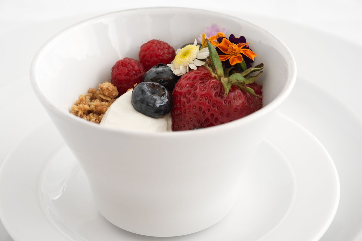 A bowl of yogurt topped with mixed berries, granola, and edible flowers.