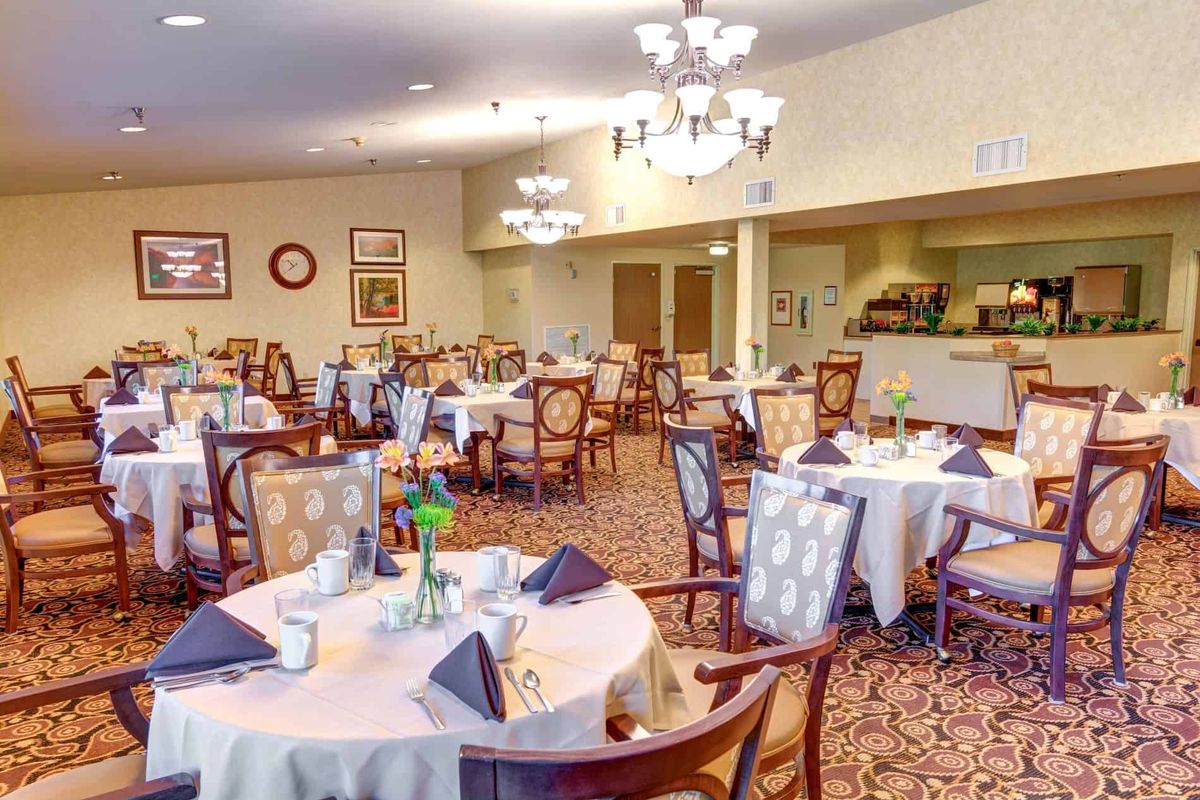An elegantly decorated dining room with round tables and upholstered chairs, featuring formal table settings and chandeliers.