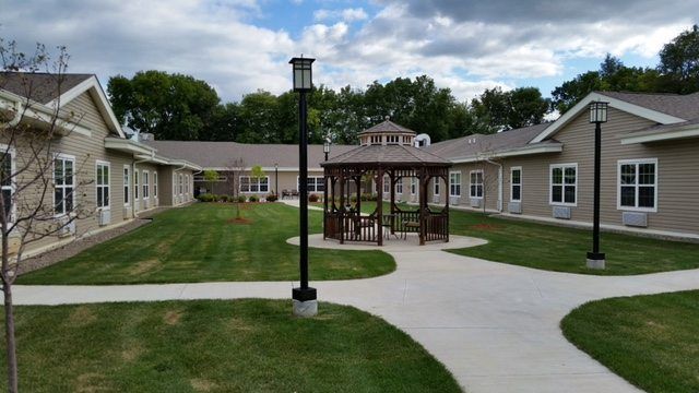 A peaceful courtyard with a gazebo, surrounded by buildings and greenery under a cloudy sky.
