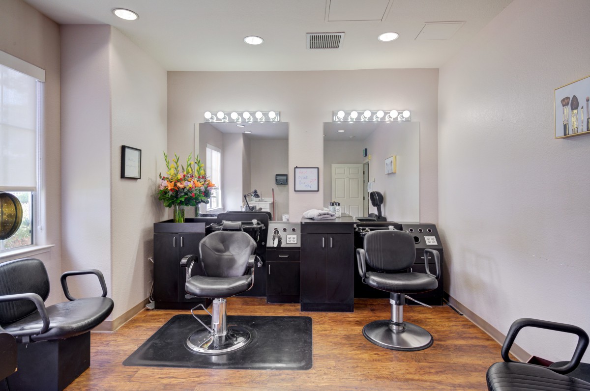 A well-lit hair salon interior featuring two styling chairs and mirrors with vanity lights.