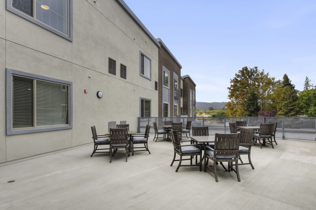 An outdoor patio with several sets of tables and chairs next to a building under a clear sky.