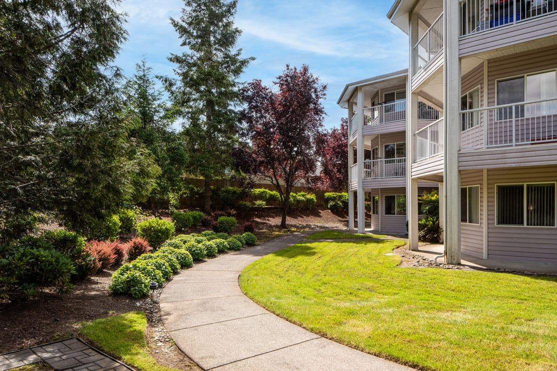 A scenic view of an apartment building with a well-maintained garden and walkway on a sunny day.
