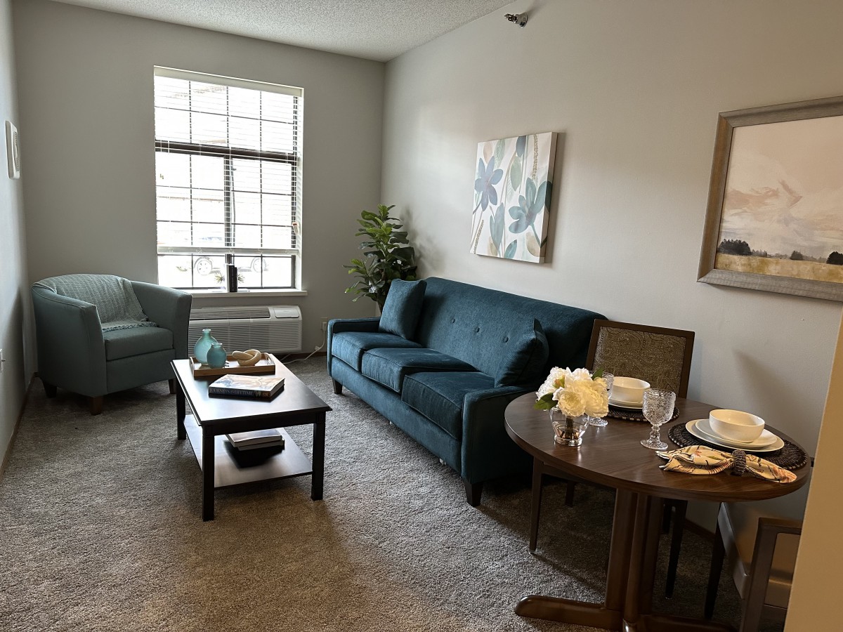 A cozy living room featuring a sofa, armchair, coffee table, and artwork on the walls.