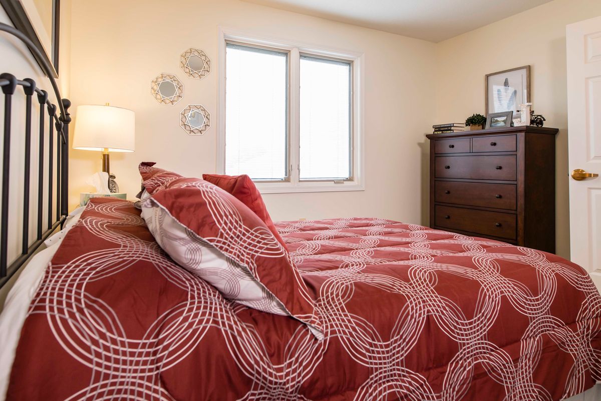 A cozy bedroom with a red and white patterned bedspread, a wooden dresser, and decorative wall plates.