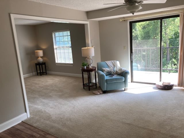 A bright living room featuring a comfortable chair, two lamps, large window, and sliding glass door.
