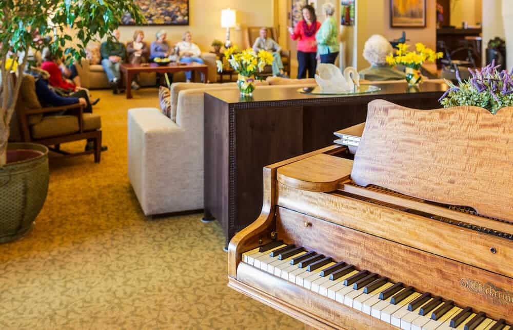 A cozy living room with a grand piano, comfortable seating, and people socializing in the background.