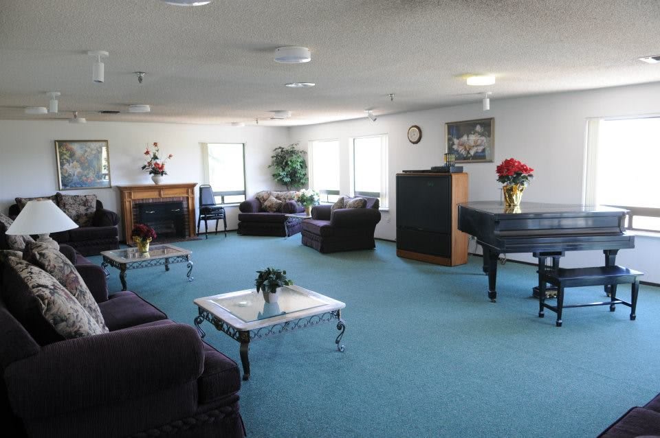 A spacious living room featuring sofas, a piano, tables, and a fireplace with blue carpet and decorative plants.