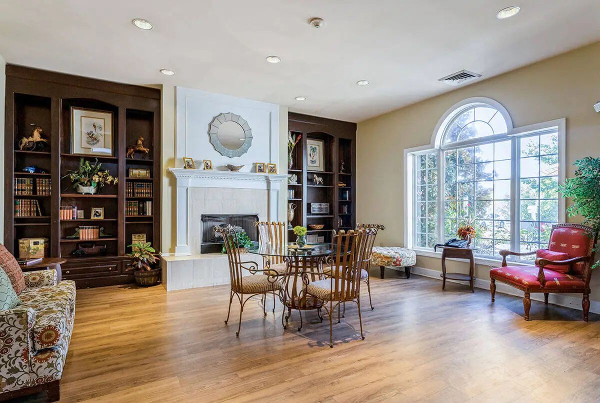 A cozy living room with a fireplace, surrounded by built-in bookshelves and a large window.