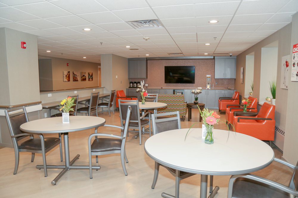 A modern lounge area featuring tables and chairs, with a TV screen and decorative vases on the tables.
