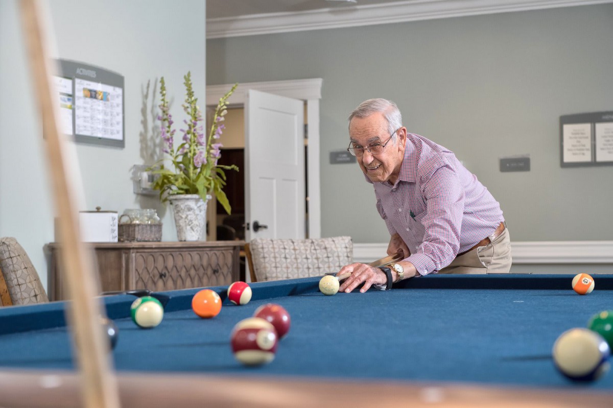 An elderly man playing billiards on a pool table in a game room setting.