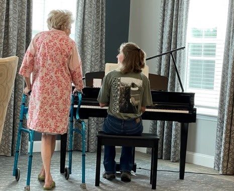 A child playing the piano while an elderly person stands nearby with a walker.