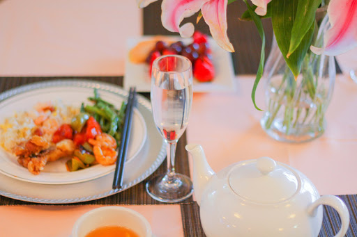A beautifully arranged dining table featuring Chinese cuisine, a teapot, and fresh fruits alongside elegant floral decor.