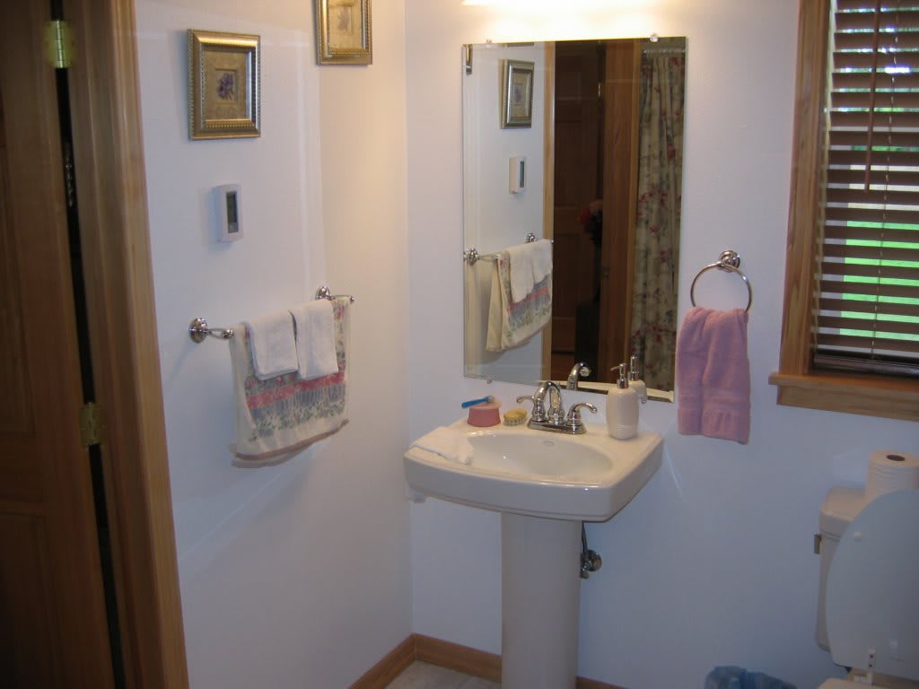 A small bathroom featuring a pedestal sink and a wall-mounted mirror, accompanied by neatly arranged towels and decorative elements.