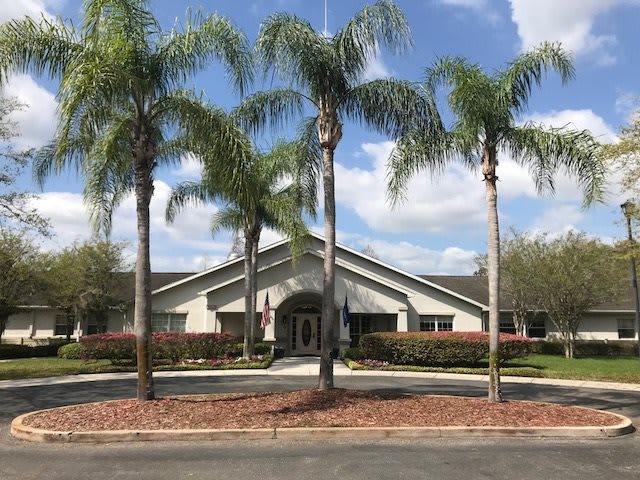 A building surrounded by palm trees under a blue sky with clouds.