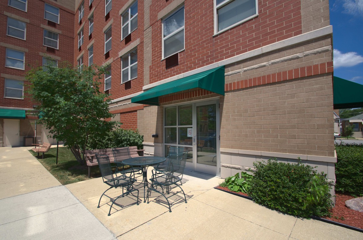 Entrance to an apartment building with outdoor seating and a green awning.