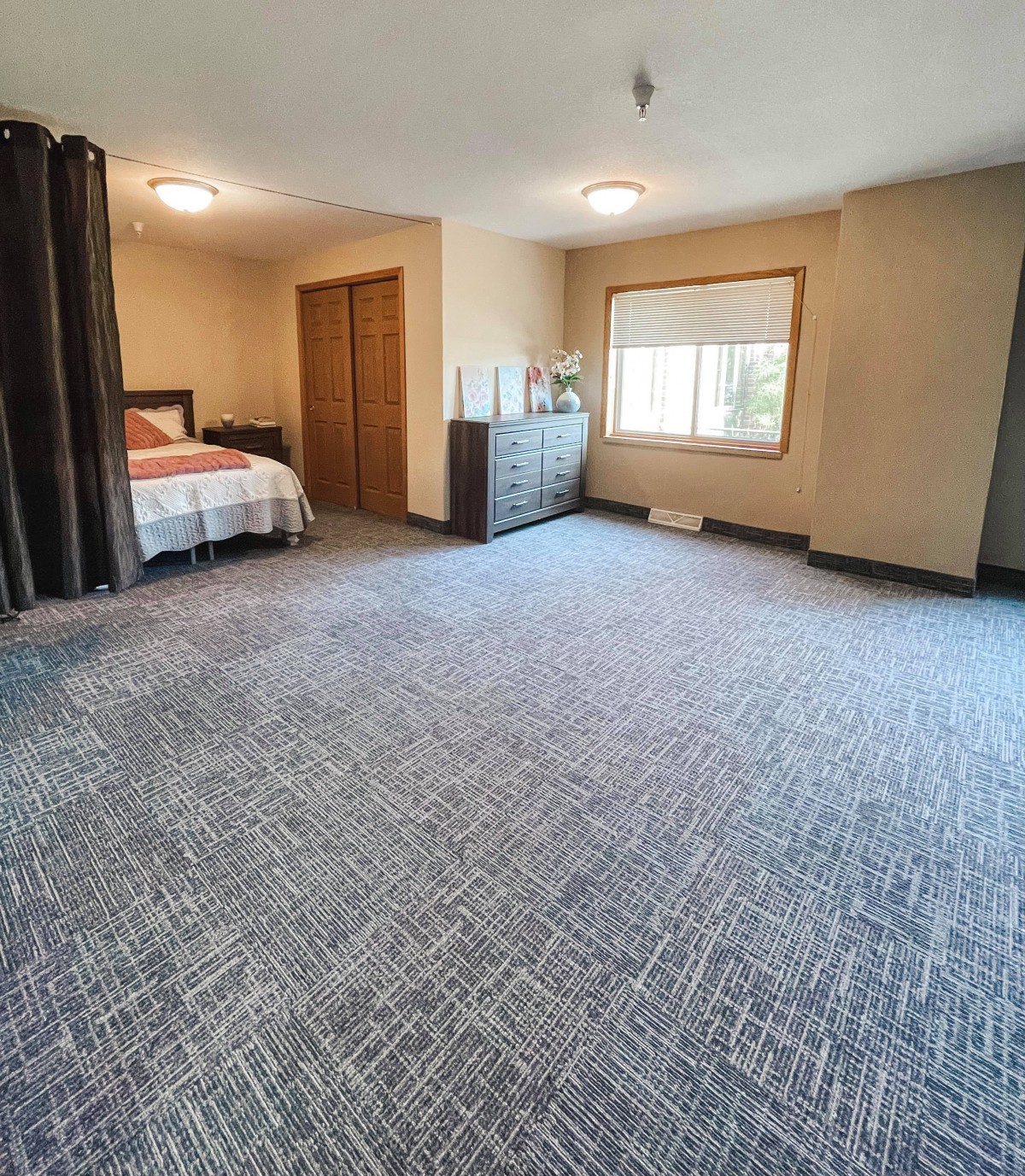 A spacious bedroom with carpeted flooring, a bed, and a dresser.
