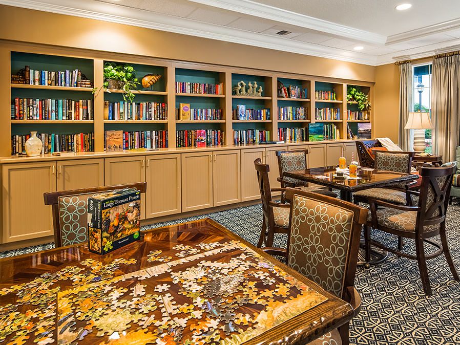 A cozy library with bookshelves, a table, and chairs, featuring a puzzle in progress.