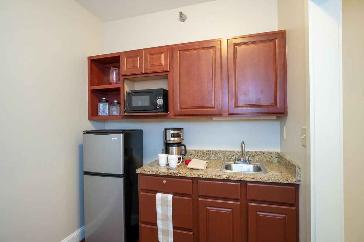 A compact kitchen area with wooden cabinets, a small refrigerator, microwave, and coffee maker.